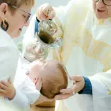 Chrzest dziecka. Kapłan polewa główkę niemowlęcia wodą święconą. Warto wiedzieć, ile kosztuje chrzest, by odpowiednio się przygotować.