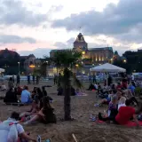 Ludzie odpoczywają na plaży, ciesząc się wieczorem. W tle widać piękne budynki, świadczące o bogactwie wydarzeń kulturalnych w Szczecinie.