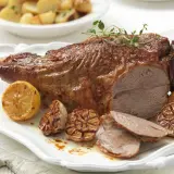 Gigot d'agneau rôti, parfumé au thym, servi avec des citrons grillés et de l'ail confit. Parfait pour une cuisson agneau barbecue réussie.