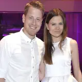 Patrycja Stockinger TTV uśmiecha się do obiektywu w białej sukience. Obok niej stoi mężczyzna w białej koszuli.