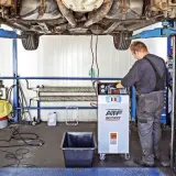 Mechanik wykonuje dynamiczną wymianę oleju w skrzyni biegów za pomocą specjalistycznego urządzenia.