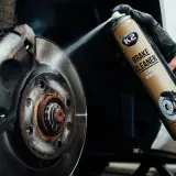 Ręka w czarnej rękawiczce rozpyla środek K2 Brake Cleaner na zużyte tarcze hamulcowe, usuwając rdzę i brud z ich rantów.