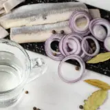 Förberedelser för inlagd sill: sillfiléer, rödlök, lagerblad, pepparkorn och en bägare med ättika. 1, 2, 3 lag.