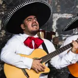 Muzycy mariachi w sombrero i białych koszulach z czerwonymi muszkami grają na gitarach.
