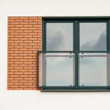Nowoczesne balkony francuskie z przeszklonymi balustradami i ceglanym detalem na białej elewacji.