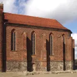 Gotycka budowla z cegły, przypominająca dawną warownię templariuszy, z charakterystyczną okrągłą wieżą i strzelistymi oknami.