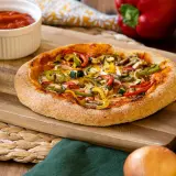 Pizza vegana con pimientos, calabacín y champiñones sobre tabla de madera. Salsa de tomate y berenjena al lado.