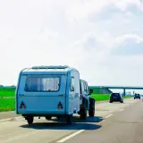 Samochód terenowy ciągnie dmc przyczepy kempingowej po autostradzie. W tle zielone pola i most.