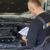 Mechanik sprawdza dokumentację przy otwartej masce samochodu. Czy wymiana oleju poza ASO a gwarancja to dobry pomysł?