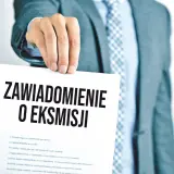 Mężczyzna w garniturze trzyma dokument z napisem "Zawiadomienie o eksmisji", sugerujący wstrzymanie eksmisji z mieszkania.