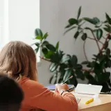 Ein Mädchen konzentriert sich auf seine Aufgaben während der Freiarbeit in der Grundschule. Ein Lehrer steht daneben.