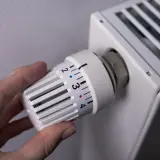 Dłoń reguluje termostat grzejnika, kontrolując ogrzewanie domu na gaz. Ustawienie temperatury na 3.