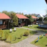 Ustronie Morskie centrum: drewniane domki z czerwonymi dachami, plac zabaw z trampoliną i piaskownicą, leżaki na trawie.
