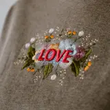 Besticktes Sweatshirt mit dem Wort "LOVE" umgeben von bunten Blumen. Zeigt, was man besticken kann.