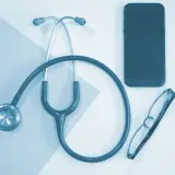 Stetoskop, okulary i telefon leżą obok siebie. To może być pomocne przy pytaniu, jak obliczyć dochód do składki zdrowotnej.