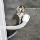 Instalacja odpływu do pralki. Wąż odpływowy podłączony do syfonu pod zlewem, na odpowiedniej wysokości.