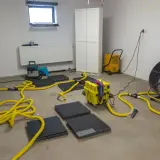 Gerät zur Trocknung eines **Wohnraums im Keller**: Bautrockner, Ventilator und Schläuche sind im Einsatz.