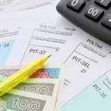 Zestaw dokumentów PIT, kalkulator, żółty długopis i polskie banknoty. Czas na rozliczenie zap-3.