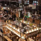 Tętniąca życiem hala Gwardii pełna stoisk z przysmakami, kawą i produktami. Ludzie spacerują, kupują i rozmawiają.