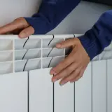 Dłonie na grzejniku, zmartwienie o rosnące ceny gazu.
