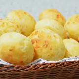 Un panier en osier déborde de délicieux pao de queijo dorés, parfaits pour un goûter.