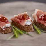 Drei kleine Brote mit Frischkäse, Feigenmarmelade und Schinken – so sieht ein köstliches Crudo aus.