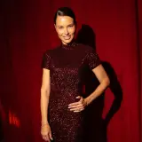 Adriana Lima actual, deslumbrante con un vestido de lentejuelas borgoña, posa con confianza ante un telón rojo.