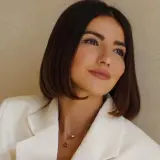 Mujer con un corte de pelo **italian bob**, blazer blanco y collares delicados.