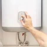 Mano ajustando el control de temperatura de un termo eléctrico.