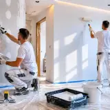 Dwóch fachowców przygotowuje ściany do malowania. Jeden szpachluje, drugi maluje. Sprawdź, jaka jest szpachlowanie cena.
