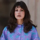Mujer con melenas cortas con volumen, flequillo y un llamativo abrigo morado y turquesa.