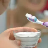 Mano tiene una spazzolino con dentifricio e una ciotola con polvere bianca, forse per sbiancare i denti con perossido di idrogeno.