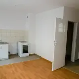 Proste mieszkanie socjalne z kuchnią: biała kuchenka, zlew, szafka i drzwi otwarte na korytarz.