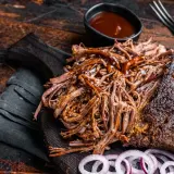 Pyszna, soczysta szarpana wołowina polana sosem BBQ, podana z krążkami cebuli na drewnianej desce.
