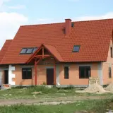 Obecny sposób zagospodarowania terenu inwestycji to budowa domu z czerwonym dachem, otoczonego materiałami budowlanymi i zielenią.