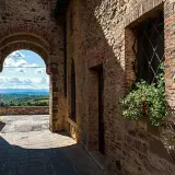 Un vicolo in pietra a San Gusmè, con un arco che rivela un paesaggio collinare toscano.