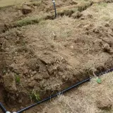 Des tranchées creusées révèlent des tuyaux noirs, prémices de réseaux enterrés pour l'irrigation ou le drainage.