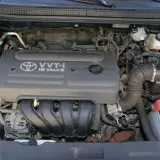 Silnik VVT-i 16 Valve z Toyoty Corolla E12. Widoczny alternator, akumulator i elementy układu dolotowego.