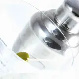 Verre à martini avec une olive, prêt pour une recette de martini gin. Shaker à cocktail en arrière-plan.