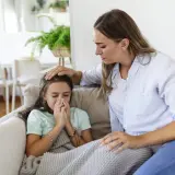 Matka troskliwie pieści czoło chorej córki, która wydmuchuje nos. Scena może budzić skojarzenia z zespołem Munchausena, gdy nadmierna uwaga skupia się na rzekomej chorobie.