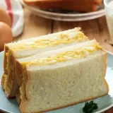 Un délicieux sandwich aux œufs, garni de pain blanc moelleux, servi sur une assiette bleue avec un verre de lait.