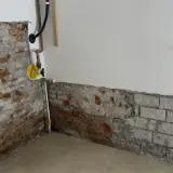 Baustelle mit freiliegendem Mauerwerk und Rohren. Ein gelbes Ventil deutet auf eine bevorstehende Maßnahme wie das Injektionsverfahren Horizontalsperre hin.