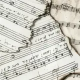 Spalone nuty z zapisem muzycznym, gdzie widać nuty i tekst. Wśród nich odnaleźć można znak bemol w muzyce, świadczący o obniżeniu dźwięku.