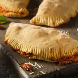 Pyszny calzone z kurczakiem, sos pomidorowy, starty ser i świeża bazylia na drewnianej desce.