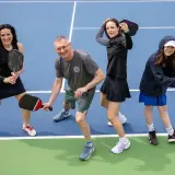 Rodzina na korcie do pickleball, co to za sport? Wszyscy trzymają rakietki, gotowi do gry.