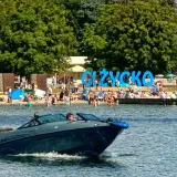 Motorówka sunie po wodzie, obok plaży w Giżycku. Idealne miejsce na odkrywanie mazurskich szlaków wodnych.
