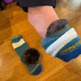 A foot wearing a fluffy-lined sock, with another striped sock and pom-pom nearby. Perfect for learning how to keep feet warm in boots.