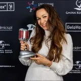 Uśmiechnięta kobieta z mikrofonem-statuetką. Jej stylizacja i nagroda sugerują, że to inspiracja dla tych, którzy chcą dowiedzieć się, jak zostać dubbingiem.