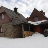 Kamienna Chatka Puchatka w Bieszczadach, zasypana śniegiem, z drewnianym zadaszeniem i stosem drewna.