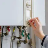 Main tenant ajuste le thermostat de sa chaudière à gaz. Une aide pour le changement de chaudière gaz est peut-être nécessaire.